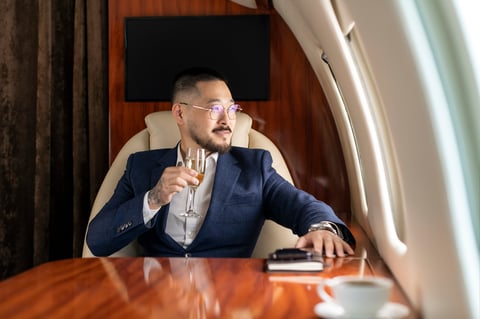 successful Asian businessman in suit and glasses sits in private jet and drinks champagne, Korean manager in business clothes flies in business class and looks out the window, luxury lifestyle