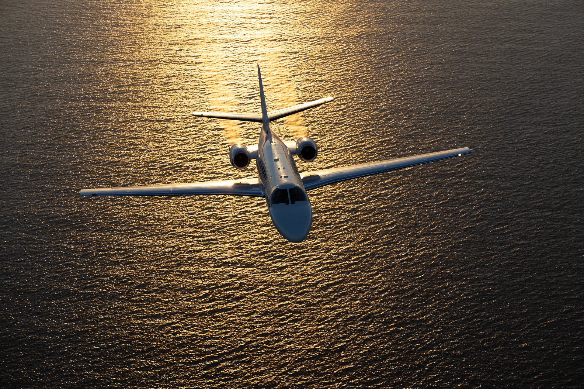 Long-range private jet in golden sunset light over the Pacific Ocean — international private jet charter worldwide