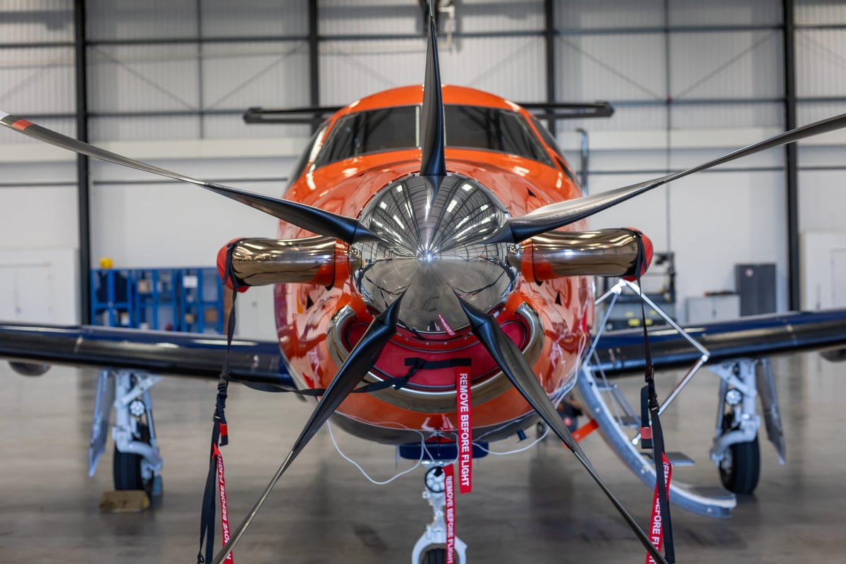 Front view of a red and yellow aircraft with propellers in an airplane hangar