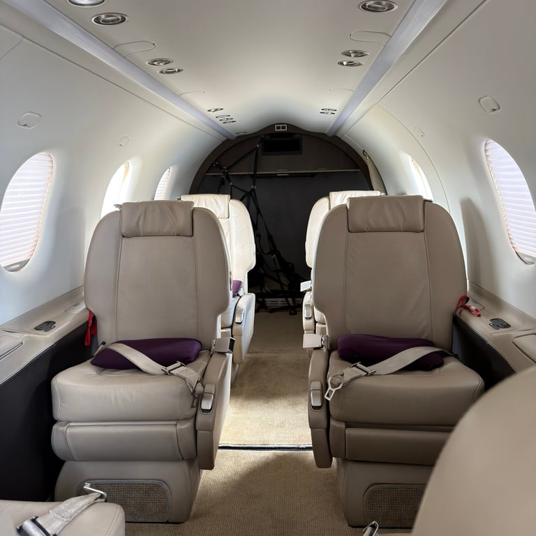 Interior of a small private aircraft cabin with beige leather seats, oval windows, and overhead lighting