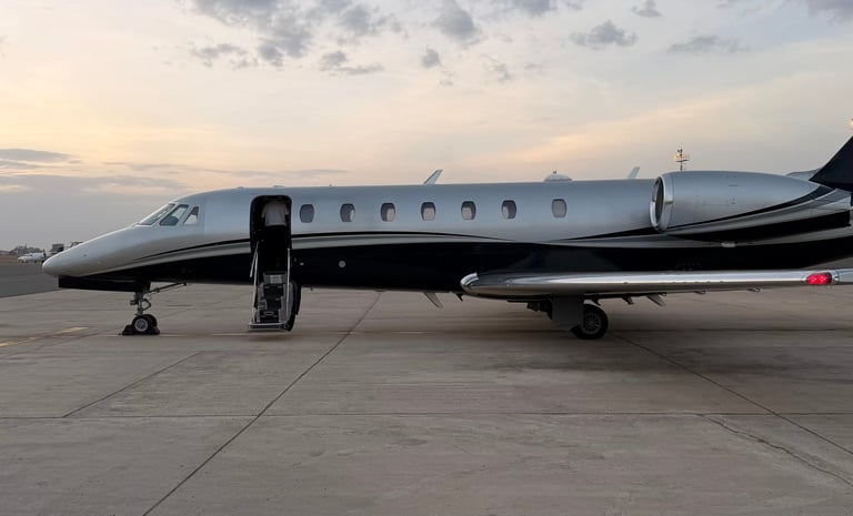 Silver and black private jet parked on runway at sunset with open door and stairs deployed