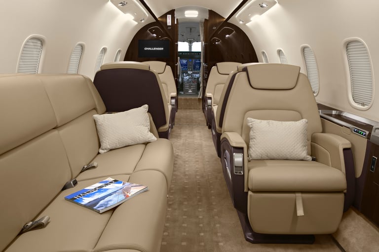 Interior of a luxury private jet cabin with tan leather seats, white pillows, and a centered aisle leading to the cockpit