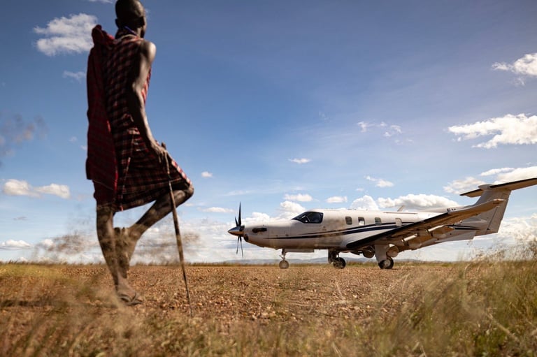 Maasai warrior standing in savanna grassland with small aircraft parked in background under blue sky