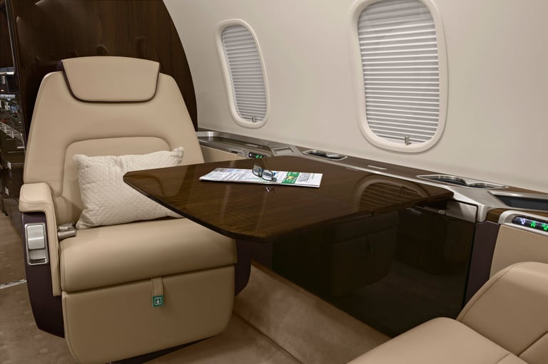 Luxury private jet cabin interior with beige leather reclining seat, dark wood table, and oval windows along the fuselage