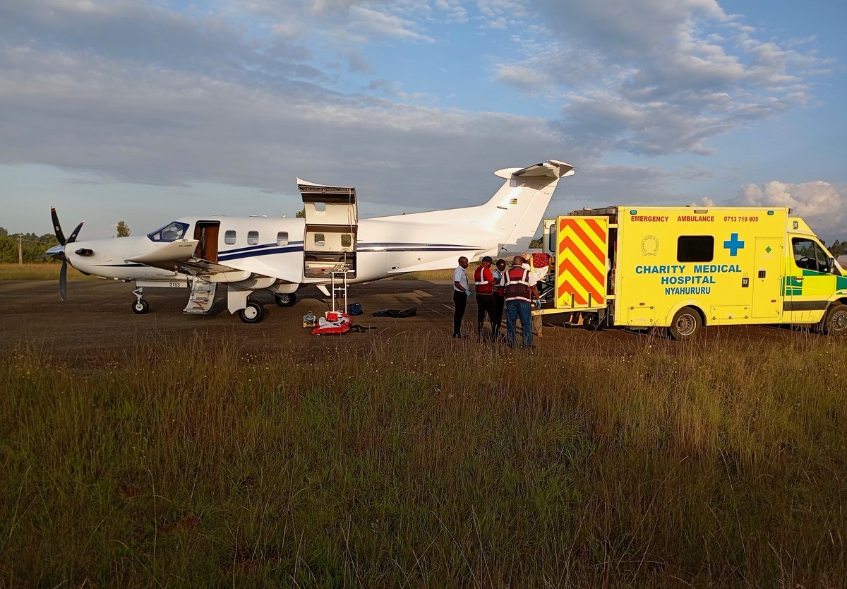 Emergency medical team loading patient into small aircraft on rural airfield with yellow ambulance nearby