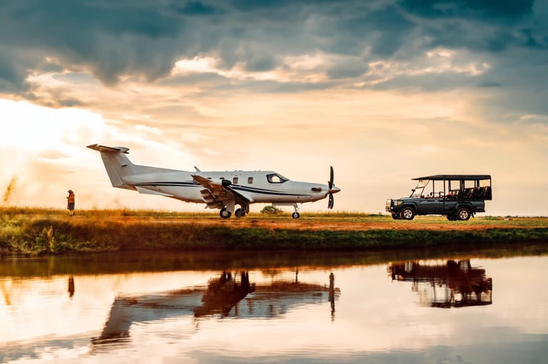 Small aircraft and safari vehicle parked by a water channel at sunset, with reflections in the water below