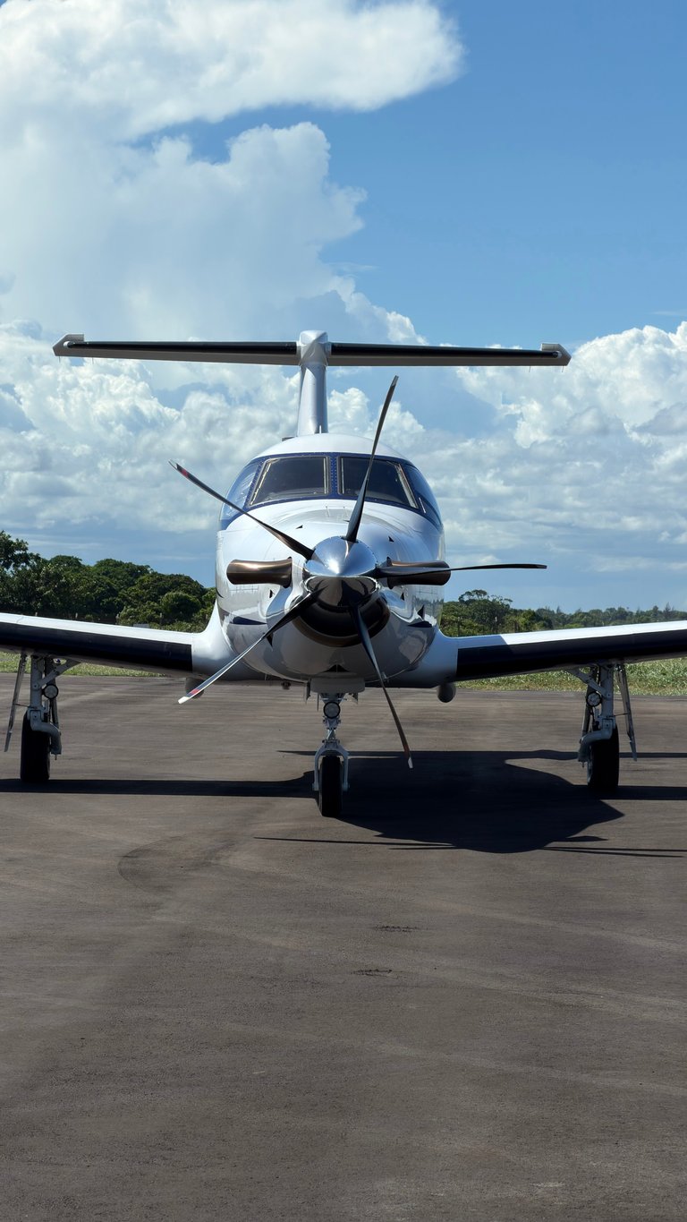 White turboprop aircraft parked on tarmac facing forward with propellers visible, cloudy sky and trees in background