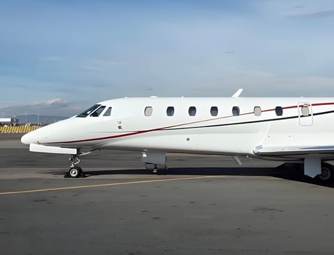 White business jet parked on airport tarmac with mountains visible in the background