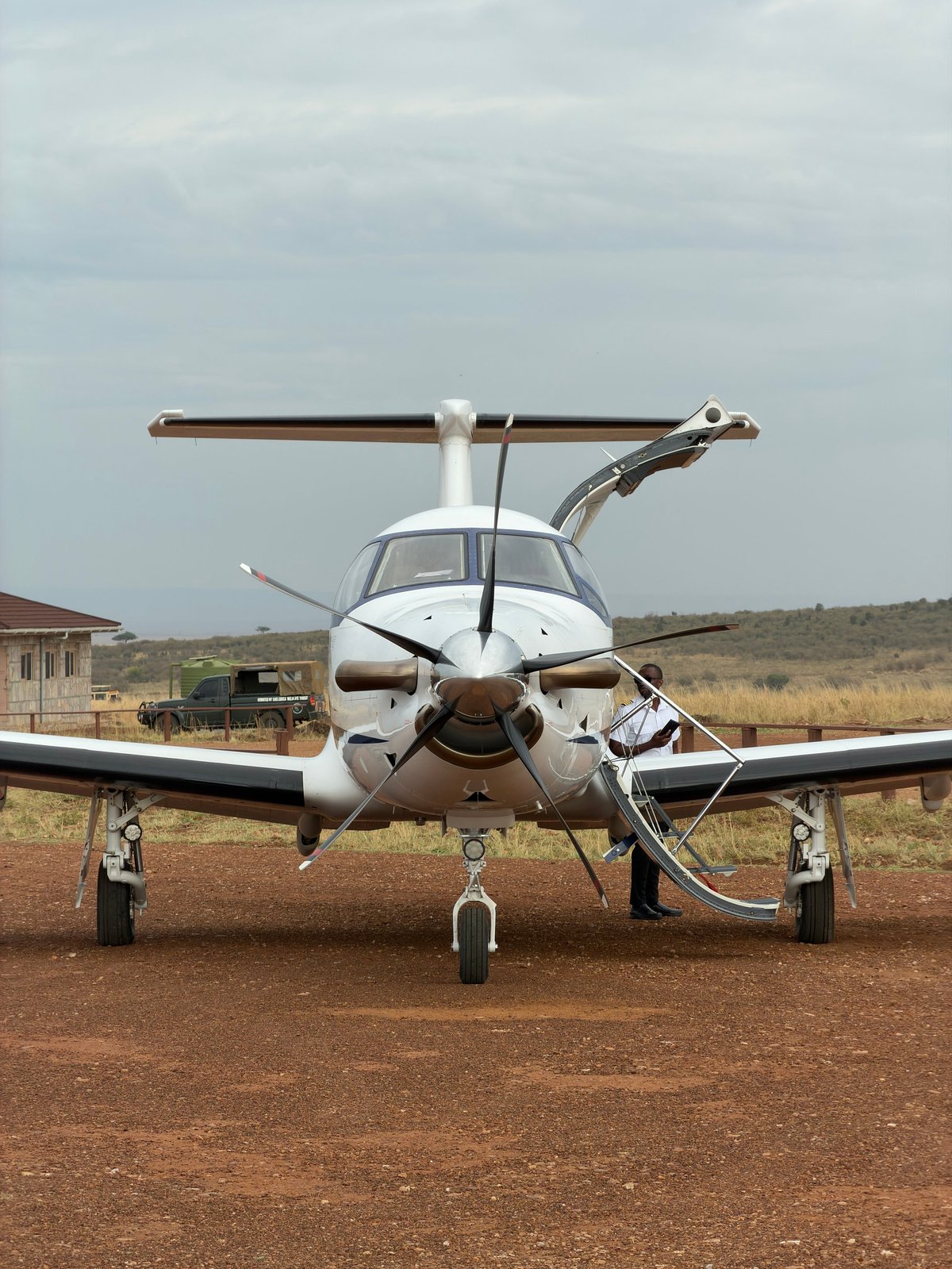 Small white and brown twin-engine aircraft parked on dirt runway with open rear door