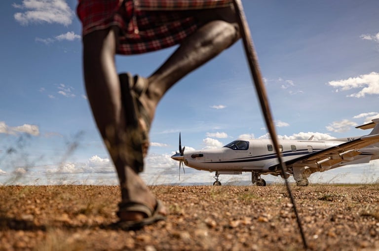 Person in red plaid shirt walking toward a small aircraft on a dusty airfield under blue sky