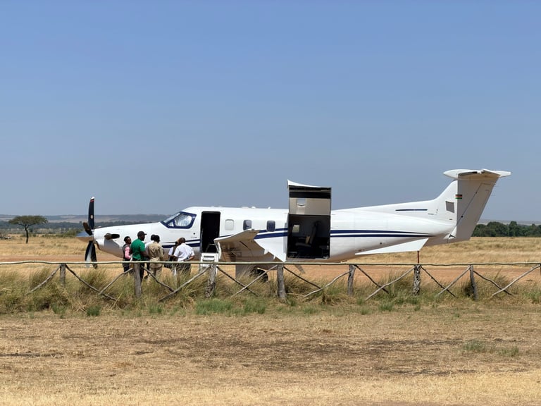 Small white aircraft on dry airstrip with people boarding, surrounded by sparse savanna landscape