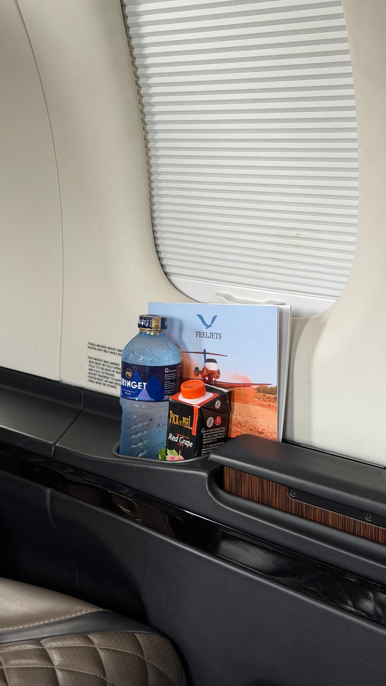 Interior of an RV showing a window with blinds, dashboard items including a water bottle, brochures, and snacks on the shelf