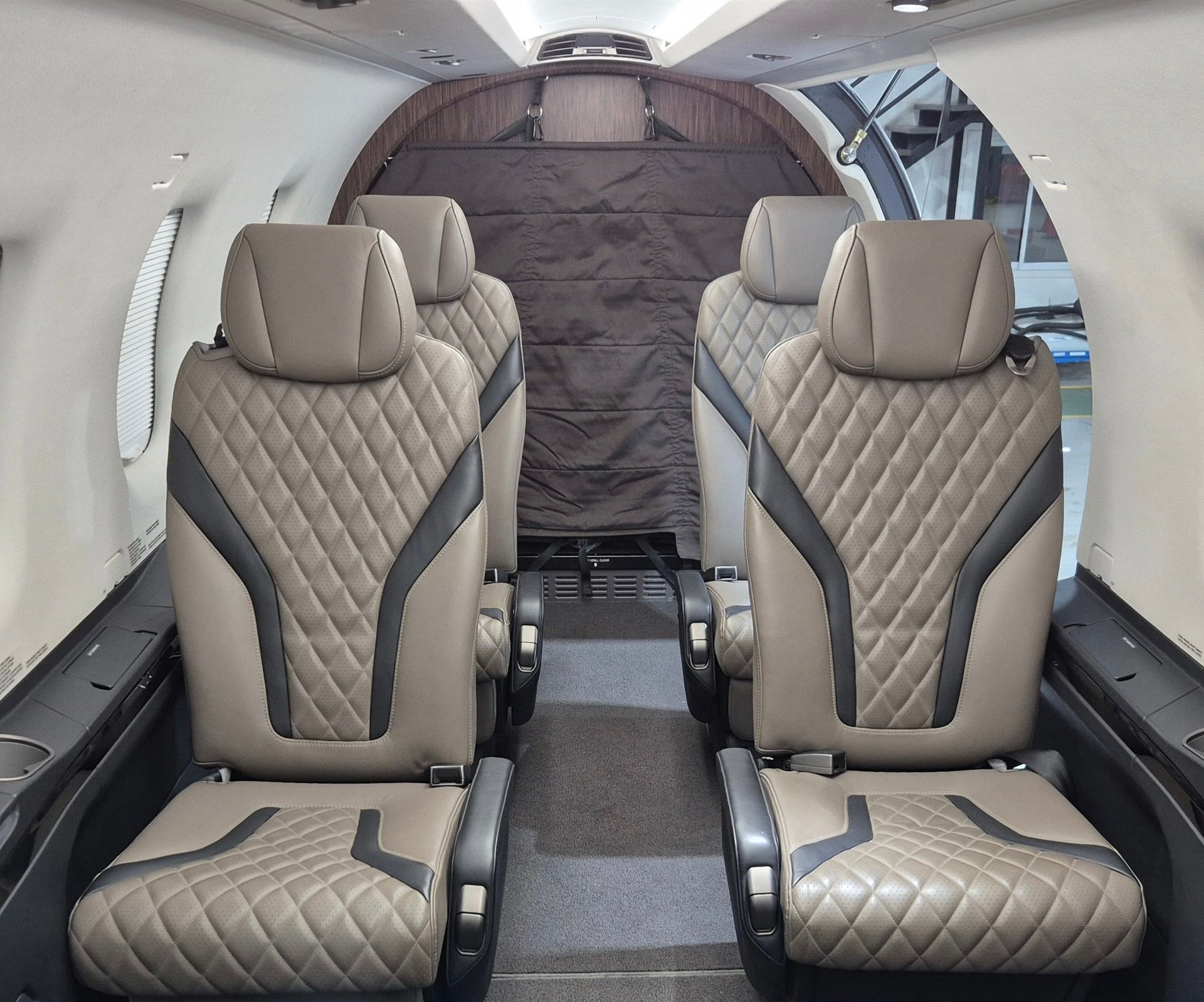 Interior of a small aircraft showing beige quilted leather seats with dark accents and gray carpeted aisle