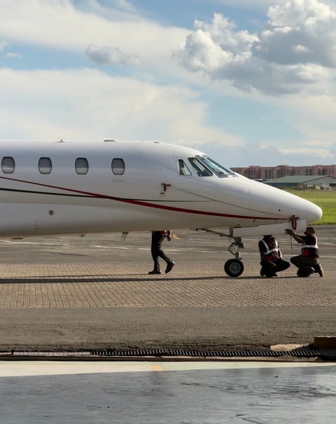 Private jet on tarmac with ground crew members performing tow operation under partly cloudy sky