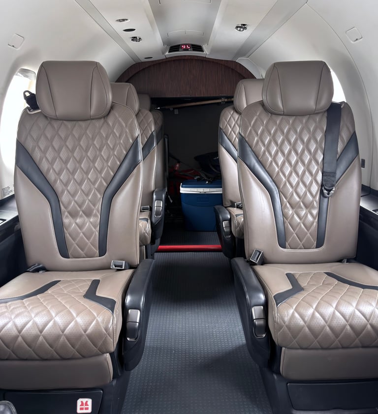 Interior of small aircraft cabin with two beige quilted leather seats and center aisle, viewed from rear toward cockpit